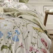 closer view: Close-up of Melodie floral duvet cover with pastel wildflowers and green stems, styled with a green throw
